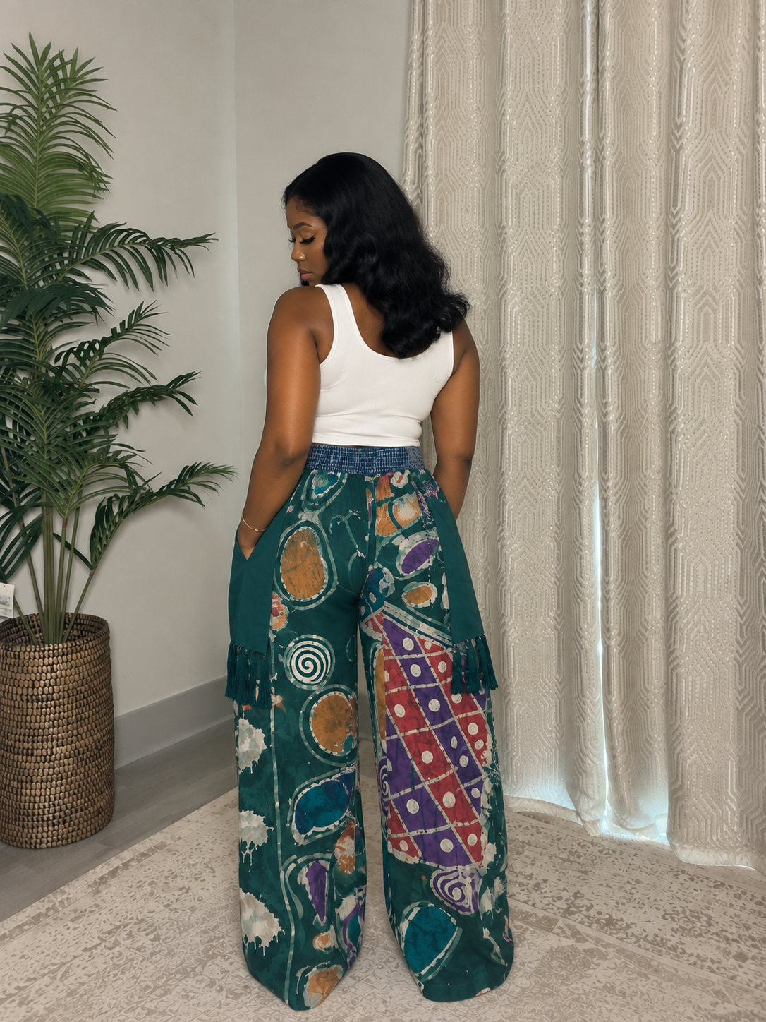 Model wearing teal batik wide-leg pants with multicolor print, layered panels and tassel details by ILÉ AYỌ̀KÁ.