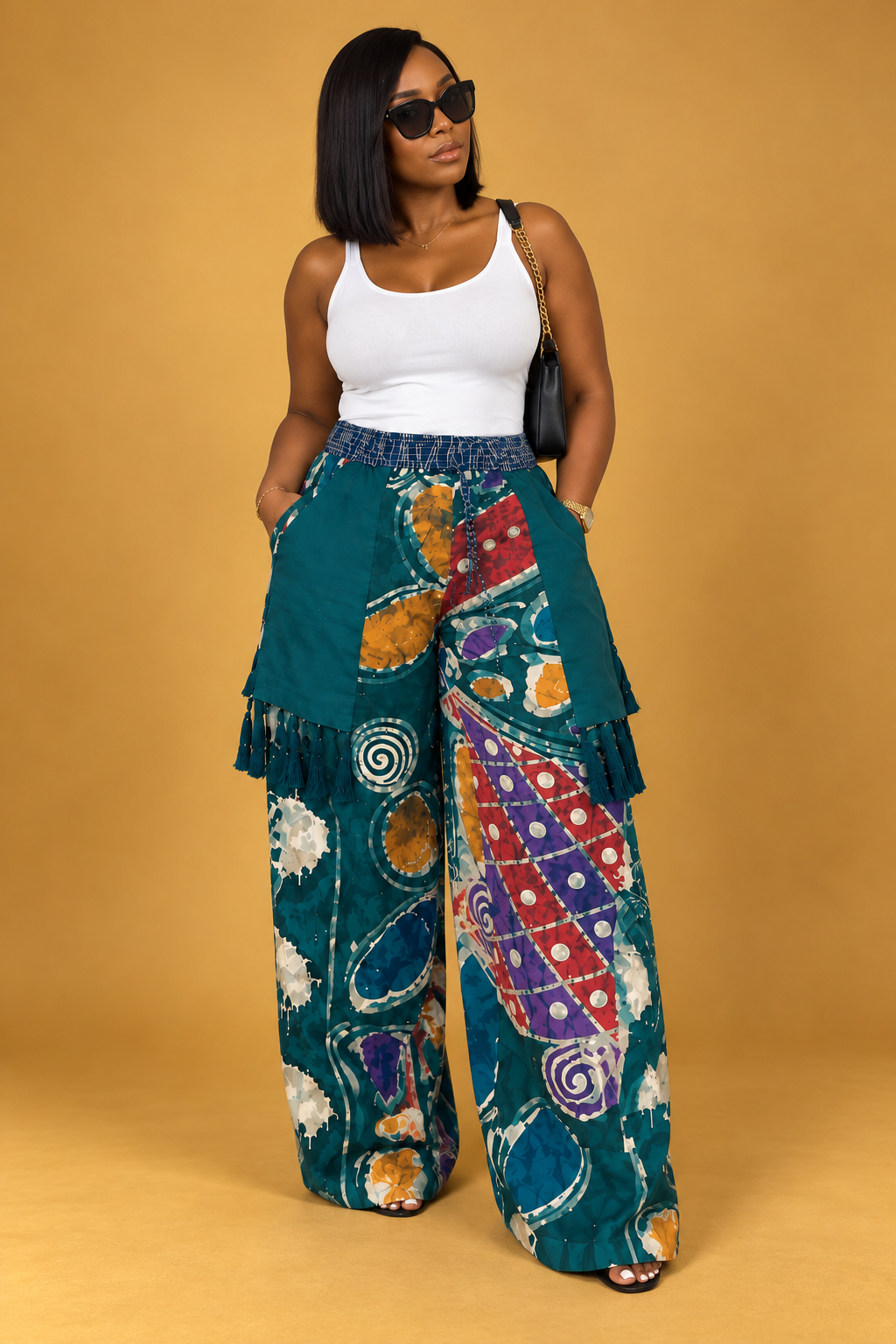 Model wearing teal adire wide-leg pants with multicolor print, layered panels and tassel details by ILÉ AYỌ̀KÁ.
