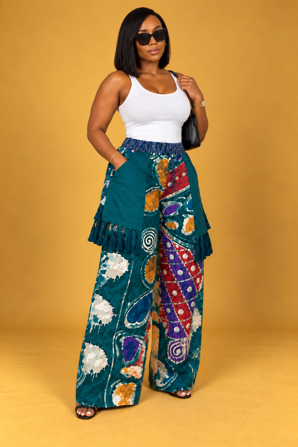 Model wearing teal Adire wide-leg pants with multicolor print, layered panels and tassel details by ILÉ AYỌ̀KÁ.